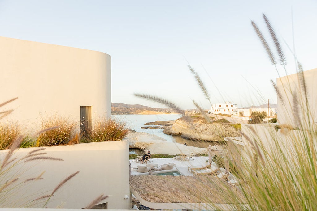 Modern luxury white suite with private infinity pool overlooking the Aegean Sea and Santorini caldera at sunset, blue domed churches below