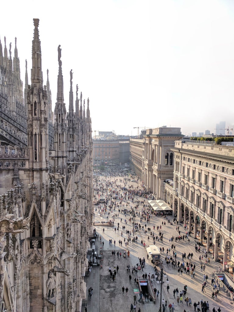 Elegant sunlit Milan Cathedral towers above Piazza del Duomo, with Gothic spires and marble facade against a clear blue Italian sky