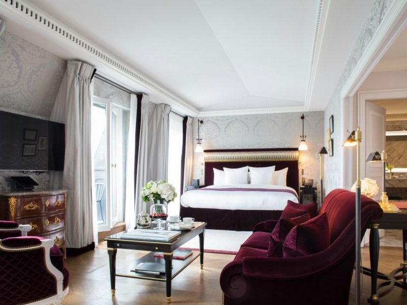 Opulent Parisian suite with crystal chandelier, gold-framed mirrors, velvet furnishings, and floor-to-ceiling windows overlooking Grand Palais