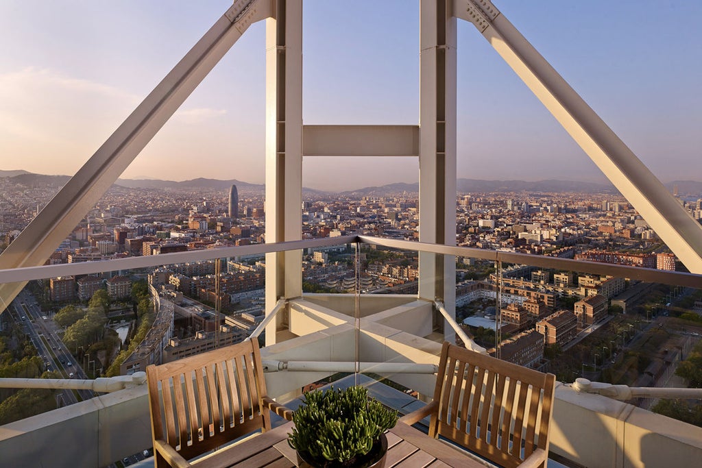 Soaring glass and steel skyscraper hotel overlooking Mediterranean Sea, with palm trees and luxury pool deck on beachfront in Barcelona