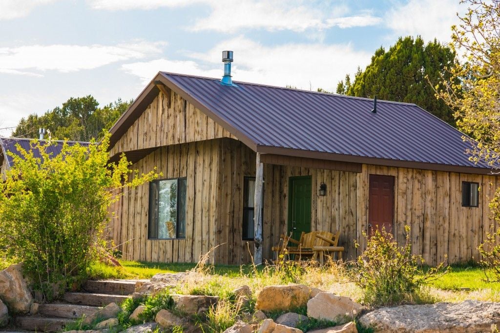 Rustic log cabin bedroom with wooden bed frame, plush bedding, and large windows overlooking scenic mountain landscape at Scenset Mountain Ranch.