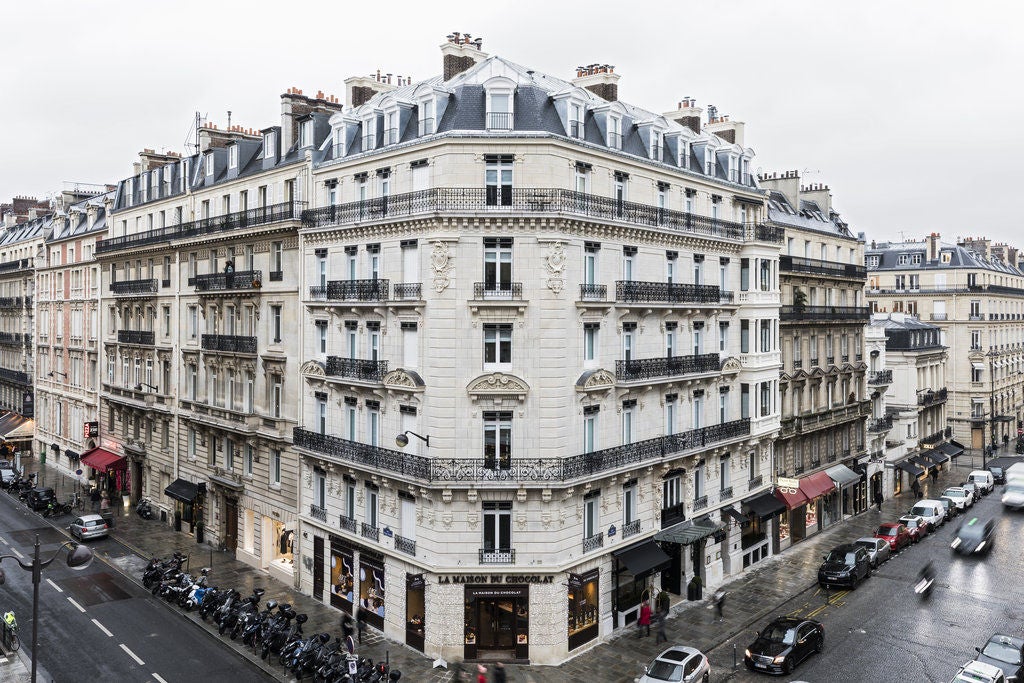 Elegant Parisian hotel facade with ornate stone architecture, wrought iron balconies, and classic French windows beneath a mansard roof