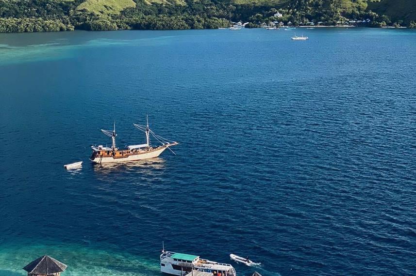 Luxurious wooden boat-hotel moored in tranquil Indonesian river, featuring expansive deck areas and traditional architectural details