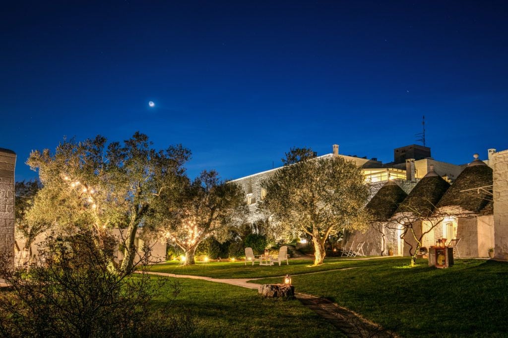 Rustic stone Masseria hotel nestled in Puglia's countryside, with elegant stone walls, terracotta roof, and lush olive grove surrounding the traditional Italian farmhouse.