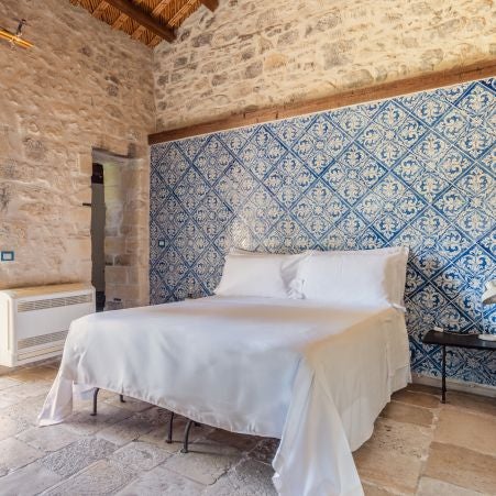 Elegant Sicilian boutique hotel room with rustic stone walls, vintage furnishings, and soft Mediterranean light filtering through arched windows