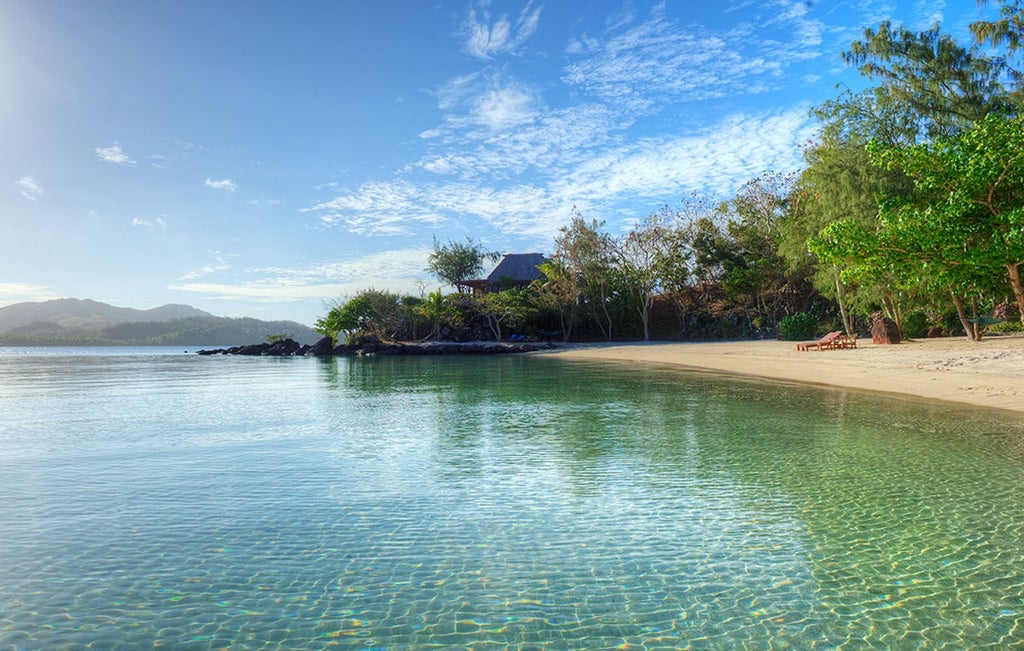 Luxurious Vonu Point Villa with wooden deck, sweeping ocean views, tropical palm trees, and elegant outdoor seating overlooking pristine Fijian coastline