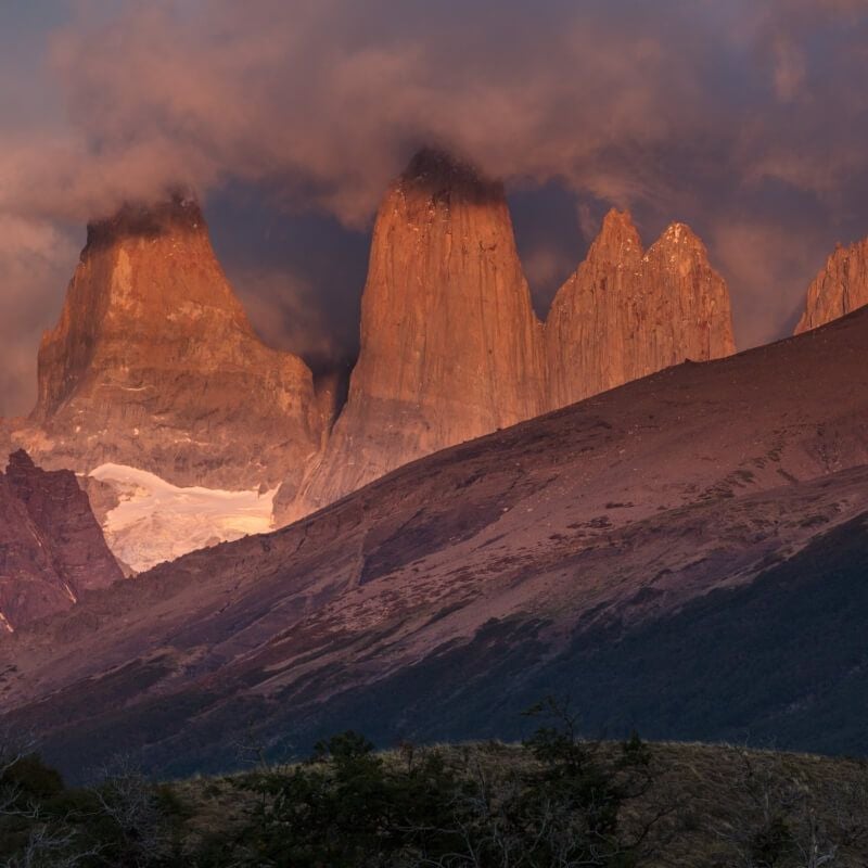 Luxurious eco-lodge nestled in rugged Patagonian landscape, rustic wooden architecture framed by dramatic snow-capped mountain peaks and windswept grasslands.