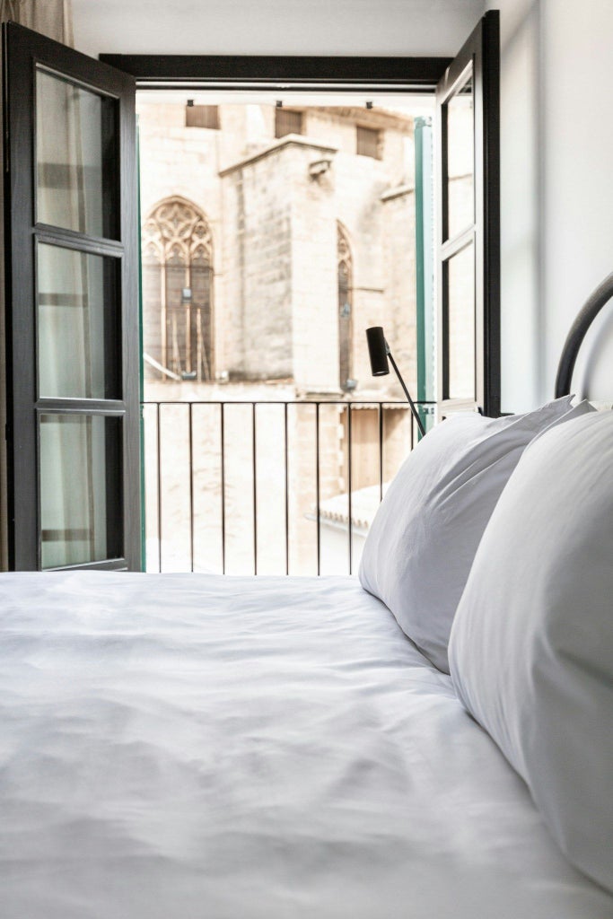 Elegant minimalist hotel room with white marble floors, plush white bedding, and expansive terrace overlooking Barcelona's historic cityscape