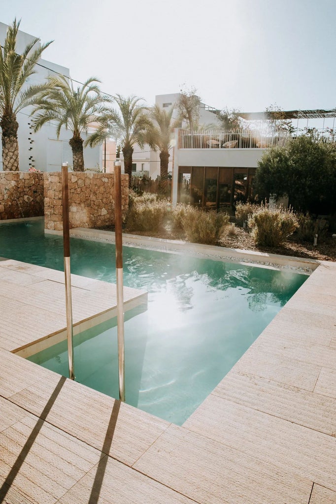 Luxurious white Mediterranean hotel with blue-tiled pool overlooking Talamanca Bay, featuring modern architecture and pristine sun-drenched coastal landscape