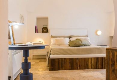 Rustic stone trulli room with elegant white linens, traditional vaulted ceiling, and minimalist decor in a luxurious Italian countryside boutique hotel