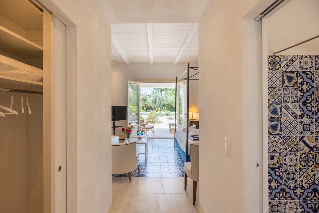 Elegant Sicilian stone-walled hotel room with refined white linens, arched window, and warm Mediterranean sunlight filtering across traditional decor