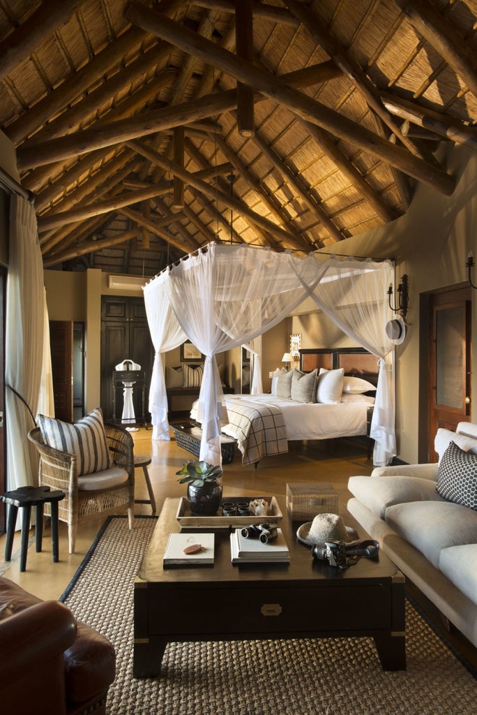 Elegant safari lodge suite with private plunge pool overlooking African bush, featuring thatched roof and wraparound wooden deck