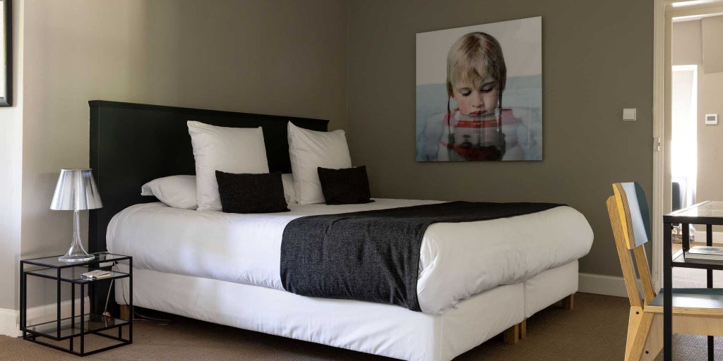 Elegant French chateau hotel room with minimalist design, white walls, contemporary furnishings, and soft natural light streaming through large windows