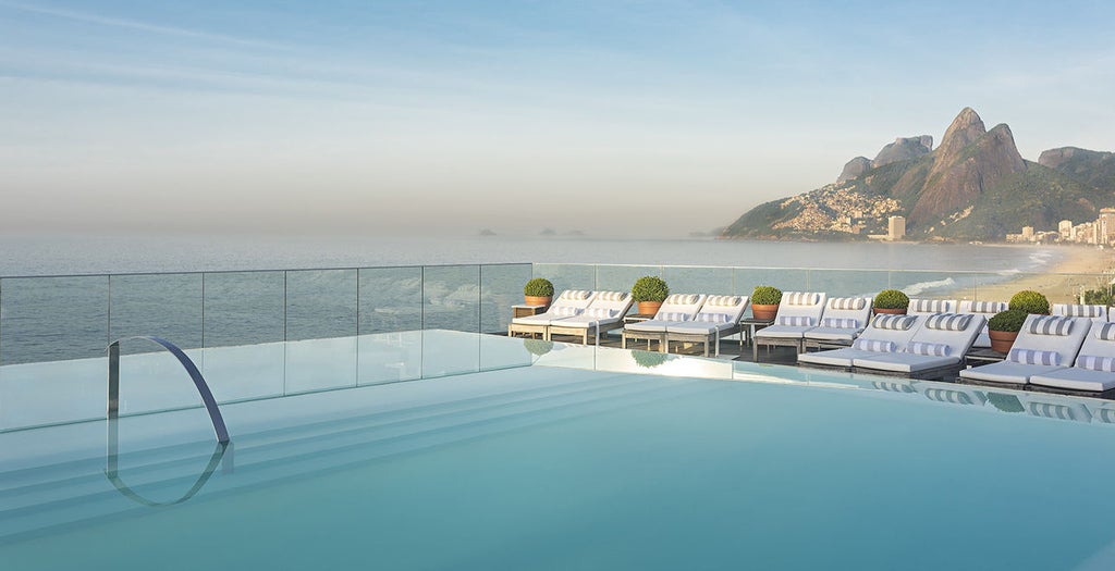 Modern beachfront hotel in Rio with infinity pool overlooking Ipanema Beach, featuring sleek glass facade and ocean-view balconies at sunset