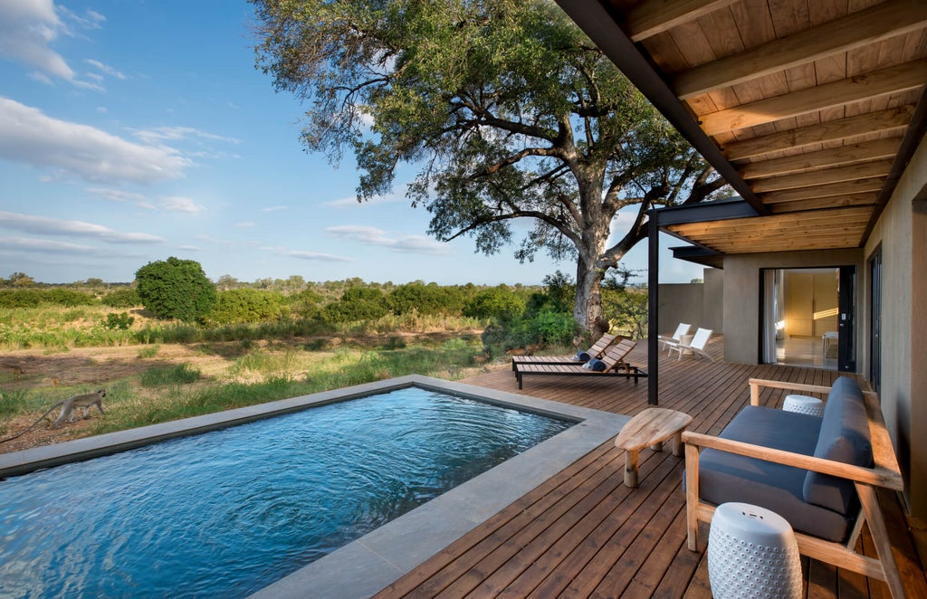 Luxurious safari lodge room with floor-to-ceiling windows overlooking African savanna, featuring modern decor and private wooden deck