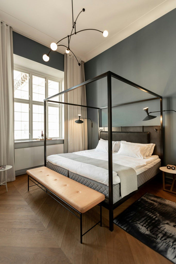 Elegant deluxe hotel room with minimalist Nordic design, soft gray color palette, plush bed, contemporary furnishings, and large windows with soft natural light in Copenhagen