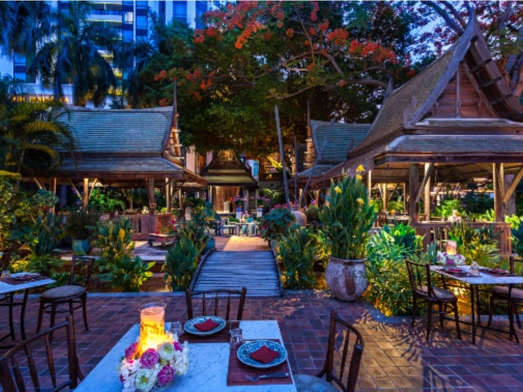 Luxury riverfront hotel in Bangkok with sleek high-rise tower, ornate traditional Thai architectural details, and palm-lined entrance