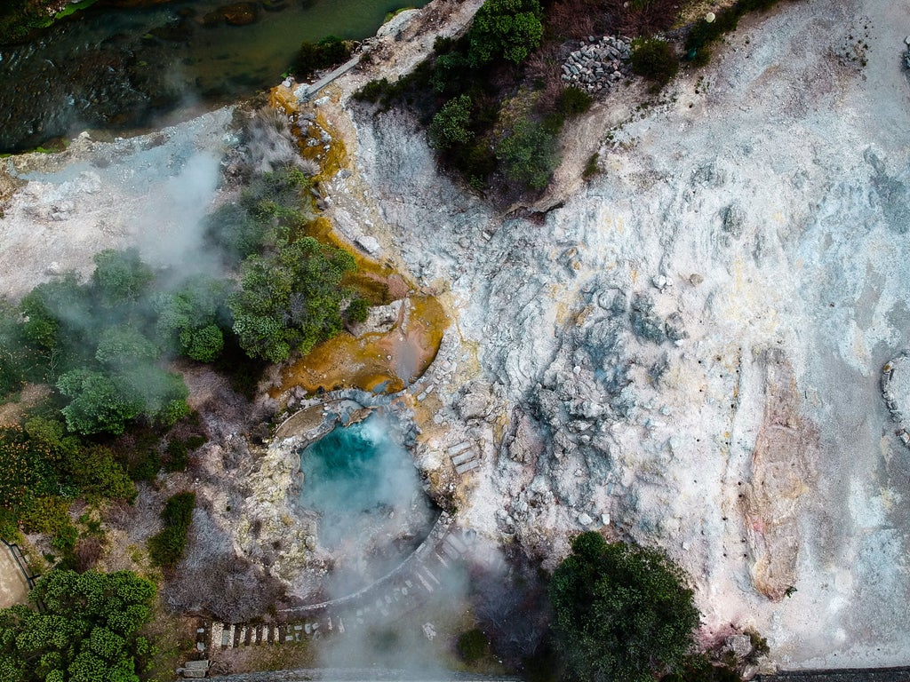 Thermal pools surrounded by lush greenery in Furnas, São Miguel, with steamy geothermal vents and traditional stone architecture in a serene landscape.