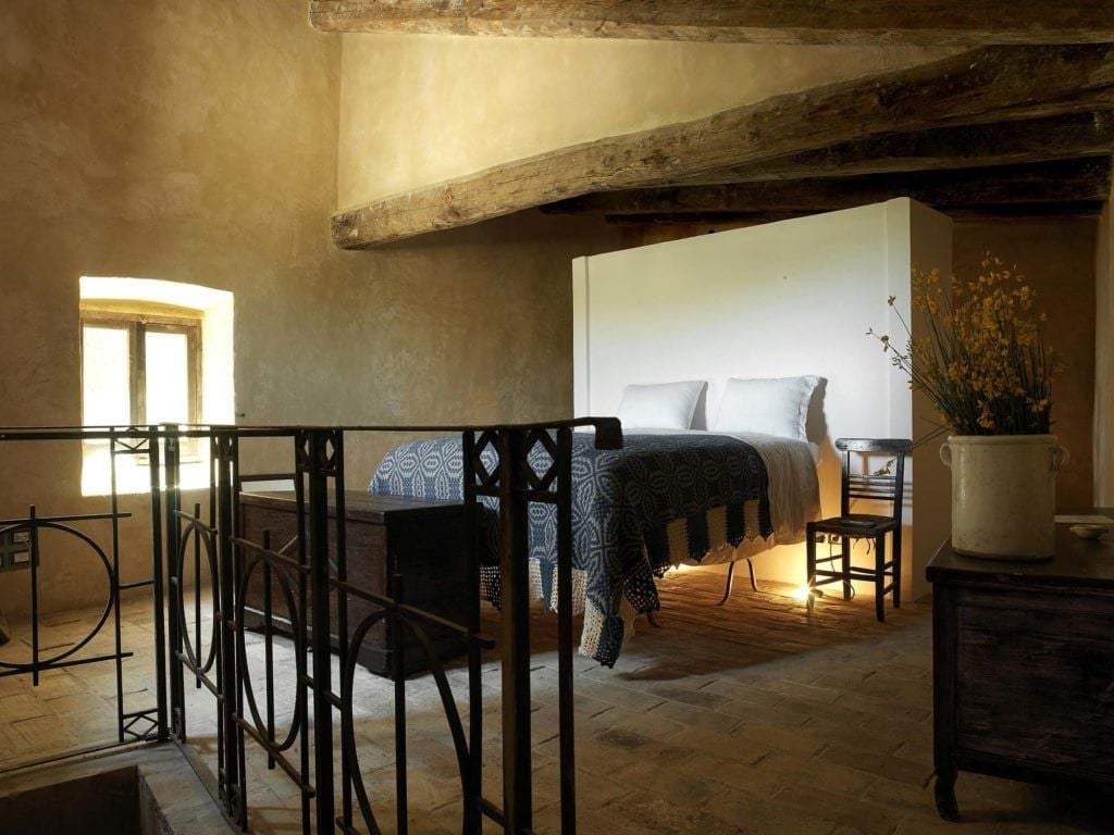 Rustic stone-walled Italian hotel room with antique wooden bed, terracotta floors, and soft candlelight, showcasing traditional scenset hospitality