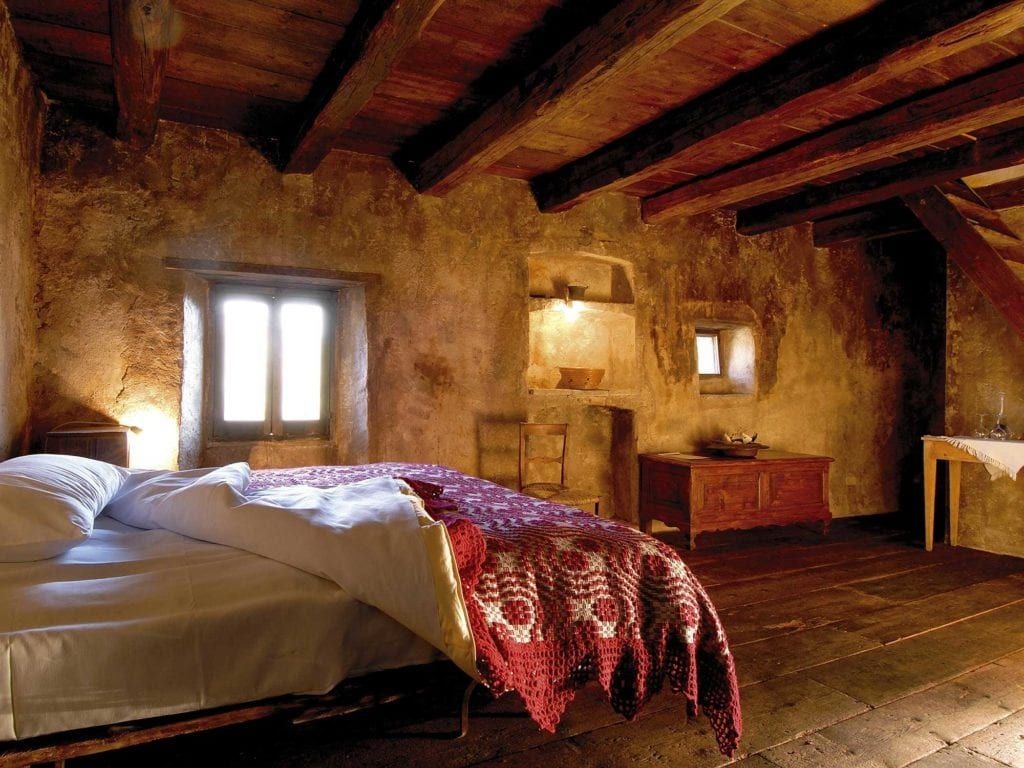 Rustic stone-walled superior room with antique wooden bed, soft linens, and traditional Italian mountain village aesthetic in soft natural light