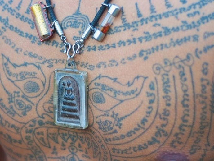 A Thai Buddha amulet worn over a Sak Yant tattoo