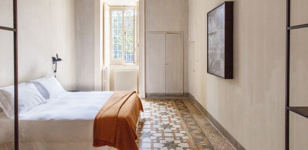 Elegant junior suite with high ceilings, ornate frescoes, and minimalist modern furnishings in a restored Italian palazzo in Puglia.