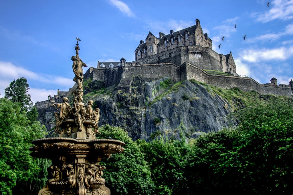 Historic Edinburgh Castle atop rocky cliff, medieval stone walls, dramatic Scottish landscape with misty skies and lush green surroundings