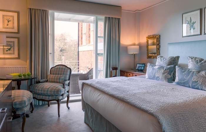 Elegant classic bedroom with soft neutral tones, plush white bedding, and refined wooden furniture at a luxury hotel in the United Kingdom.