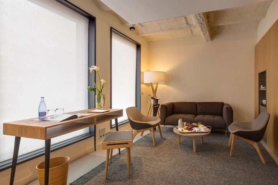 Modern, sleek hotel room at Ohla Eixample with minimalist design, white decor, plush bed, and floor-to-ceiling window overlooking Barcelona cityscape