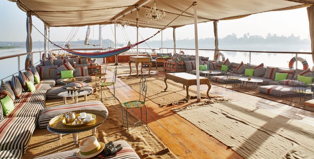 Traditional wooden Dahabiya boat with ornate blue and white details moored on the Nile, featuring elegant deck loungers and billowing white canopies