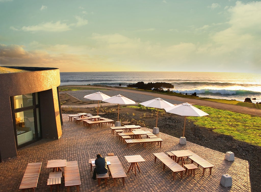 Modern luxury resort overlooking Pacific Ocean, featuring curved rooflines, native stone walls and lush gardens on Easter Island's coast