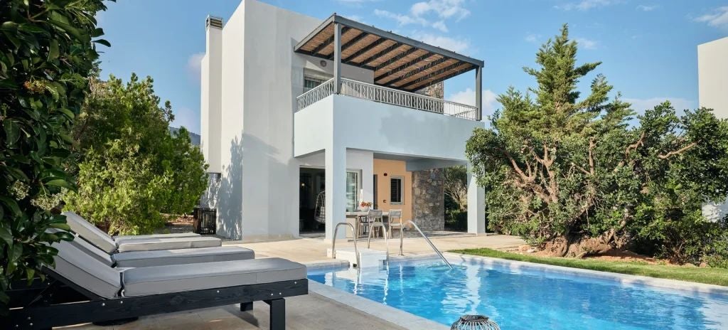 Luxurious family suite with private outdoor jacuzzi overlooking azure Aegean waters, elegant white domed architecture, and scenic Cretan landscape