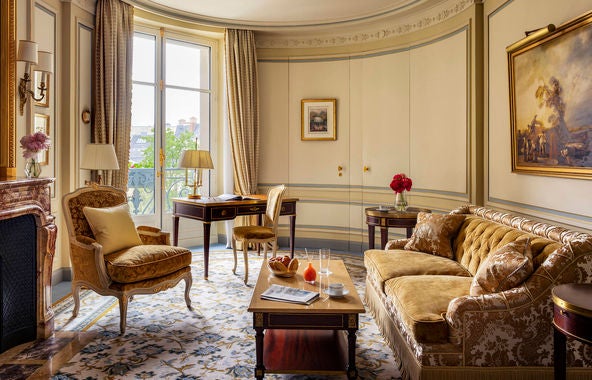 Opulent Parisian suite with crystal chandelier, ornate gold-framed mirror, silk curtains, antique furniture and plush king bed in warm tones