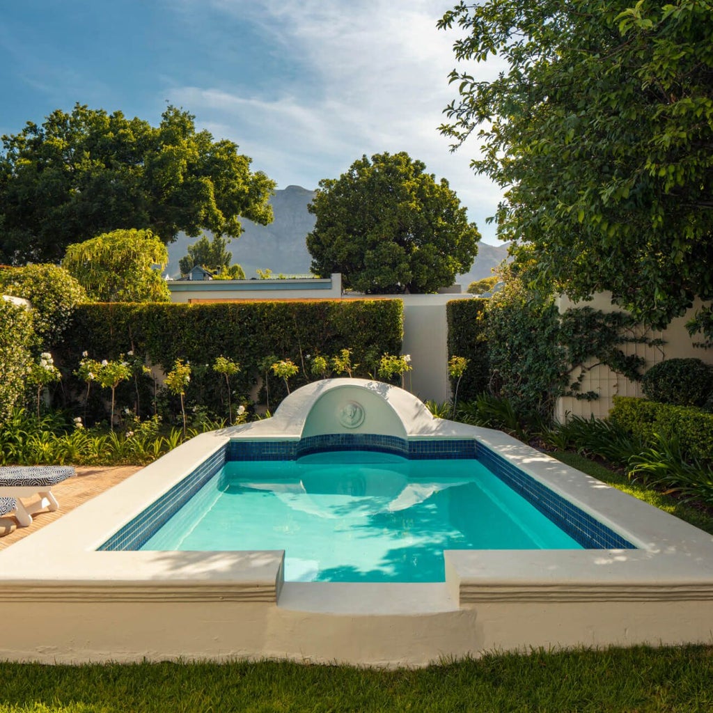 Elegant Cape Dutch-style luxury boutique hotel nestled in scenic Franschhoek, with manicured gardens, white walls, and lush mountain backdrop at golden hour