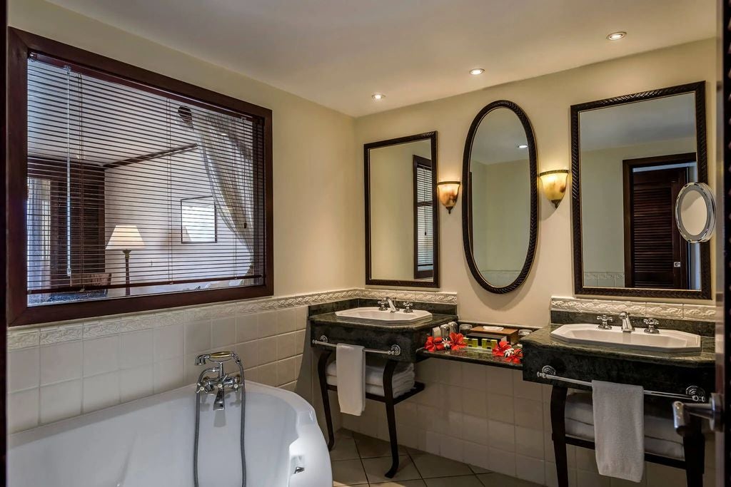 Spacious oceanfront hotel room with king bed, white linens, dark wood furniture, and floor-to-ceiling windows framing Tahitian lagoon views