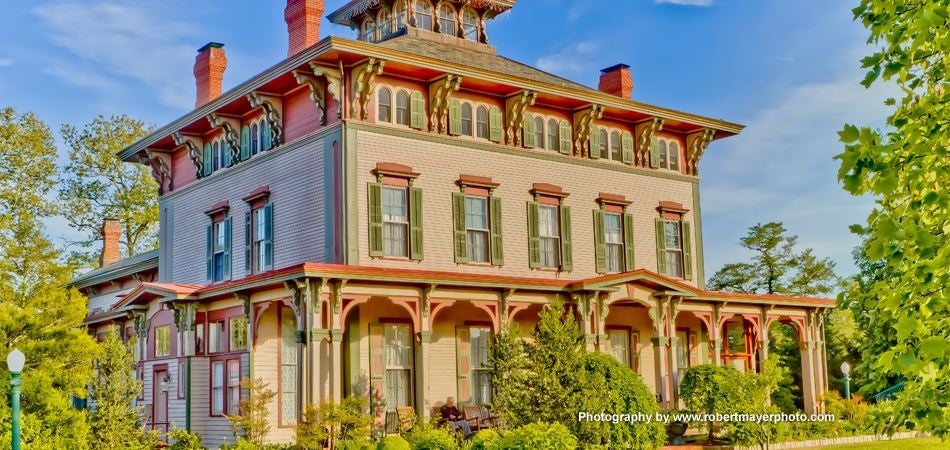 Elegant white antebellum mansion with grand columns, wrap-around veranda, and manicured gardens set against a backdrop of towering oak trees