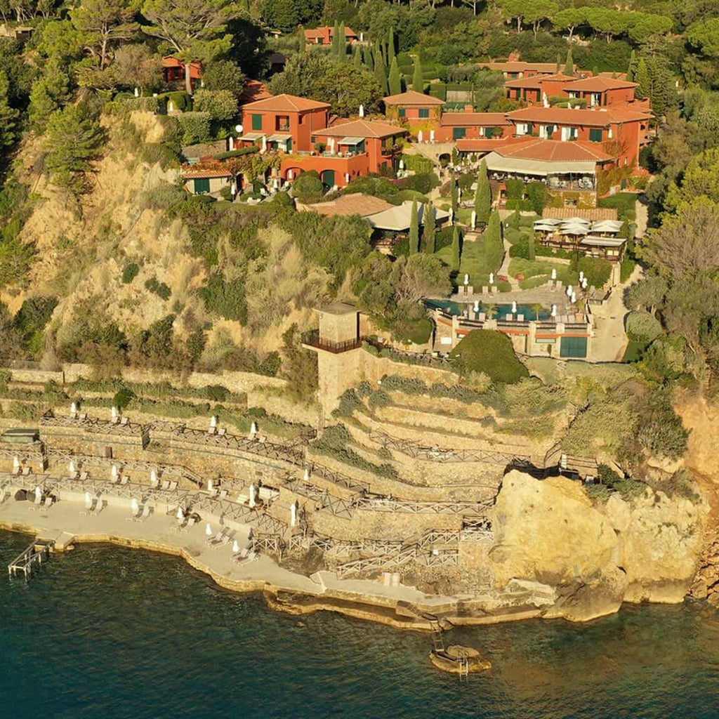 Luxurious cliffside hotel in Porto Ercole, with terracotta buildings cascading down to a private beach cove on the Tuscan coast