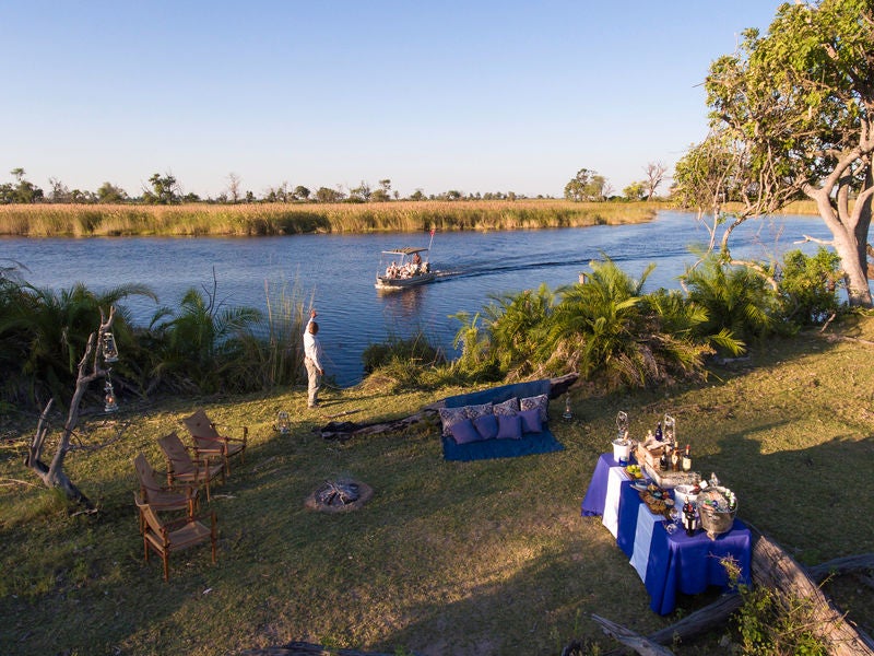 Elevated luxury safari lodge with wooden deck overlooking Okavango Delta waters, surrounded by palm trees and lush vegetation