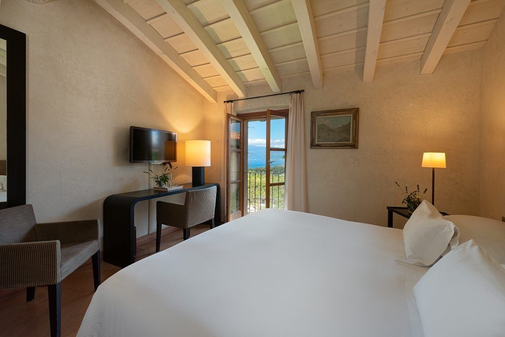 Elegant Italian lakeside hotel room with classic decor, plush white bedding, panoramic lake view, and warm wooden furnishings at Villa Arcadio