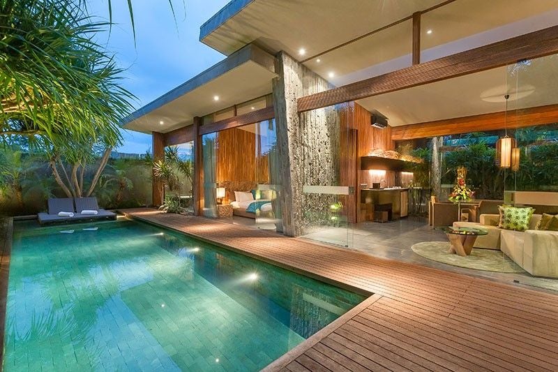 Luxury villa in tropical setting with private infinity pool overlooking lush jungle, modern glass and wood architecture at sunset