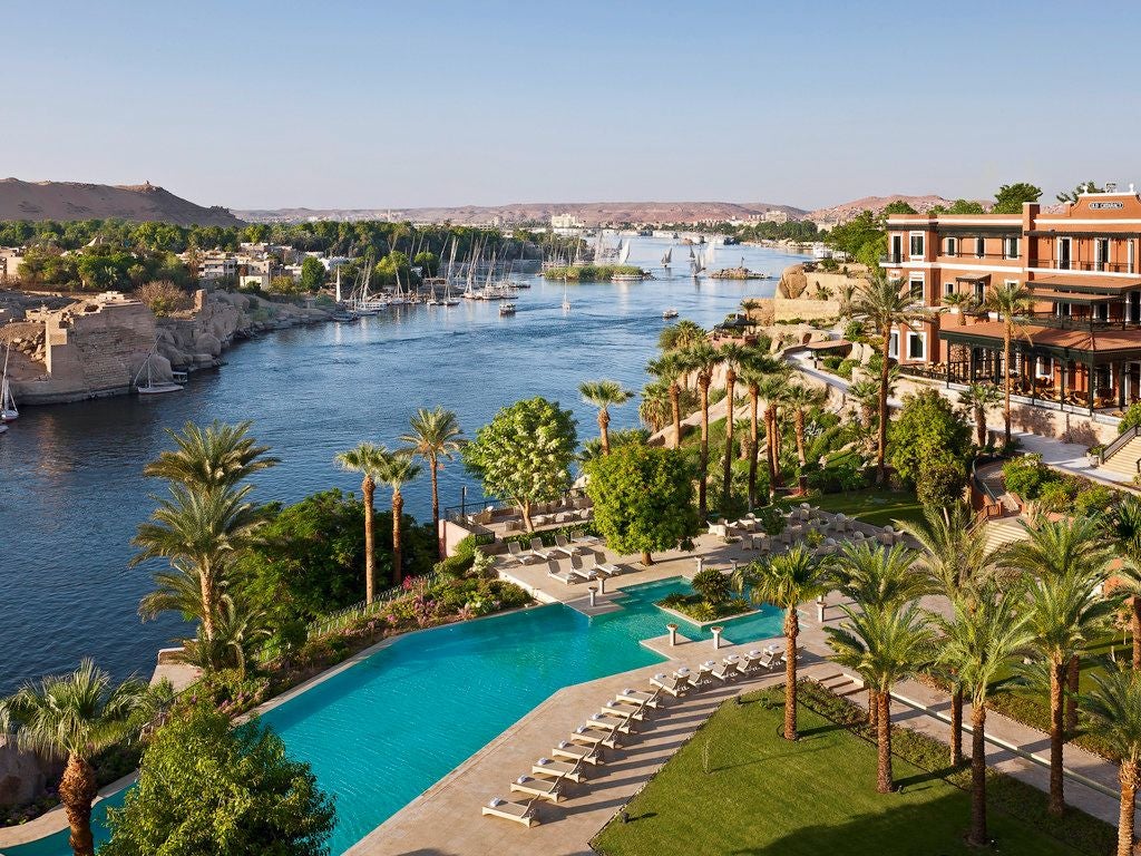 Elegant colonial-era luxury hotel perched on Nile River's edge, featuring ornate Victorian architecture with desert landscape backdrop in Aswan, Egypt