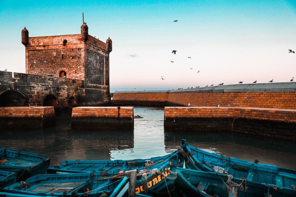 Whitewashed seaside buildings in Essaouira, Morocco with traditional blue doors, boats in harbor, and historic rampart walls