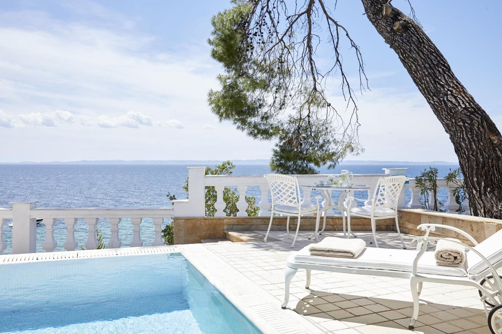 Luxurious honeymoon suite overlooking Aegean Sea, featuring private infinity pool, elegant white decor, and panoramic views of Greek coastal landscape at sunset