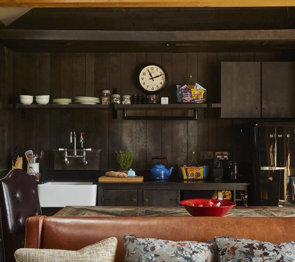 Luxurious forest cabin suite at Lime Wood, featuring rustic wood paneling, plush bedding, and large windows overlooking lush woodland scenery in the United Kingdom.