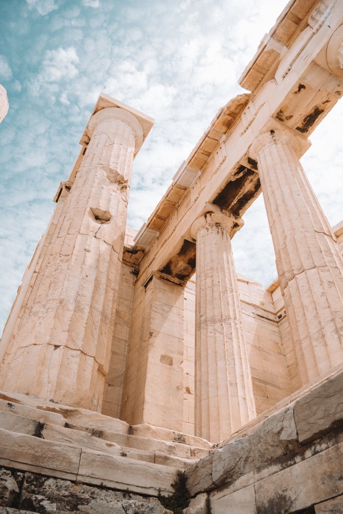 Ancient Parthenon temple atop Acropolis hill glows golden at sunset, with elegant marble columns and classical Greek architecture