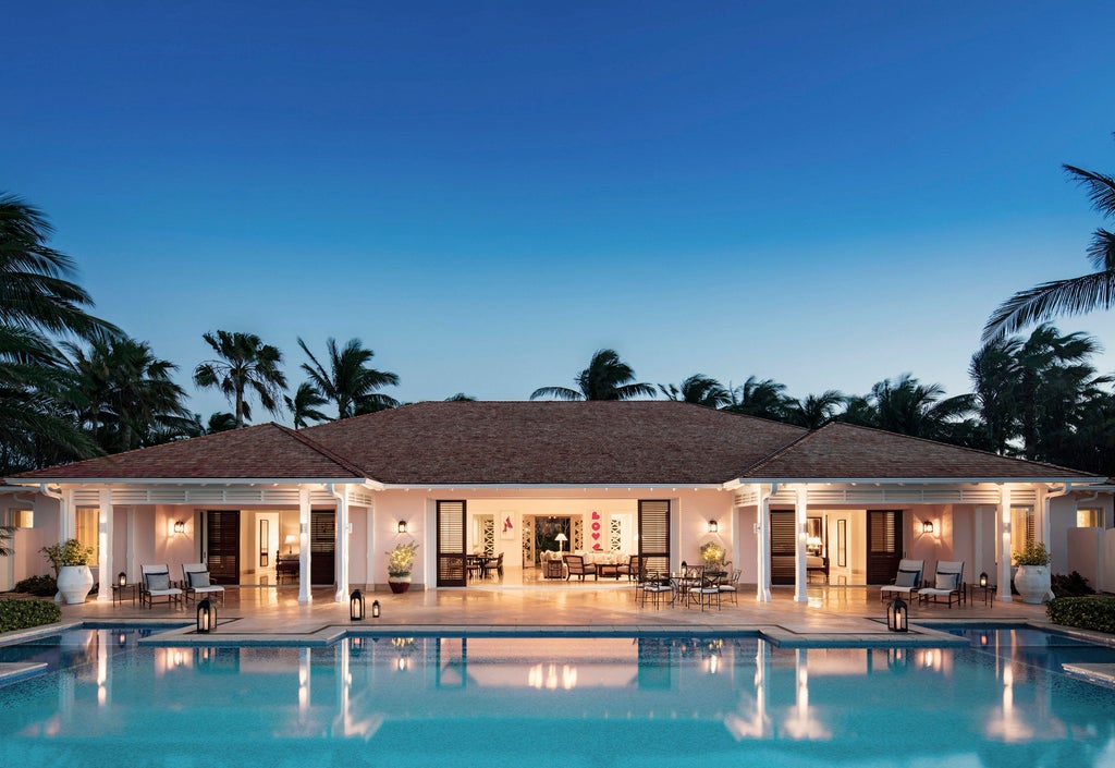 Oceanfront Four Seasons resort in Bahamas featuring white sand beach, infinity pool with loungers, and swaying palm trees at sunset