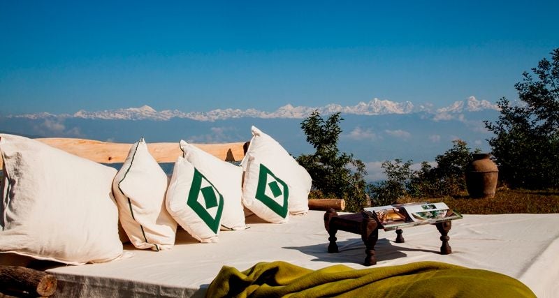 Traditional Nepali luxury hotel with ornate wooden architecture perched on hillside, overlooking misty Himalayan mountain ranges