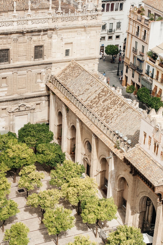 Majestic Gothic cathedral in Seville with intricate stone facade, panoramic city skyline, and golden afternoon sunlight illuminating ornate architectural details