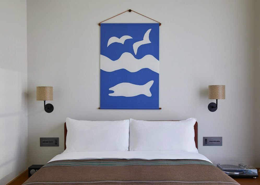 Elegant king bed with crisp white linens in modern Ace Hotel room, featuring dark wood furnishings and floor-to-ceiling windows