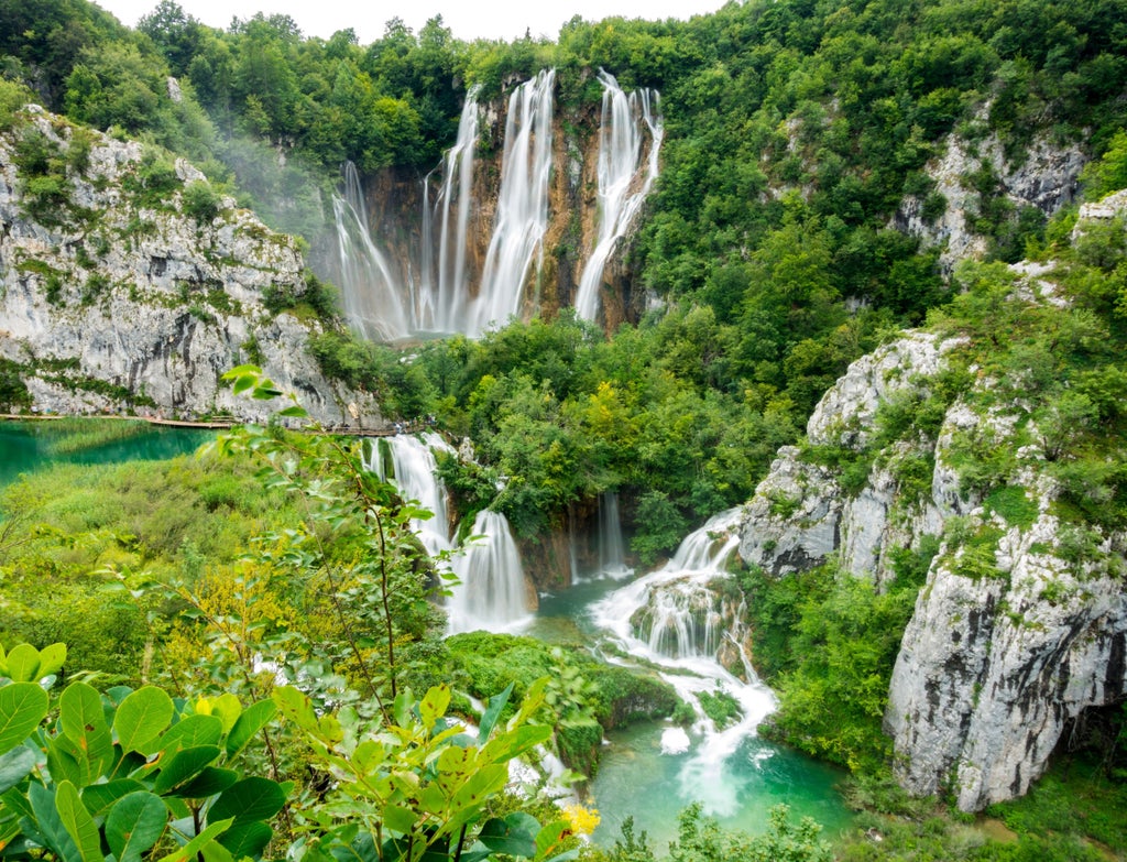 Wooden boardwalk winding through turquoise lakes and cascading waterfalls in Plitvice Lakes, surrounded by lush autumn foliage